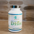 A white bottle of Natural D-Hist dietary supplement by Ortho Molecular Products, featuring a silver cap and a white label with green and blue text, set against a blurred wooden background.