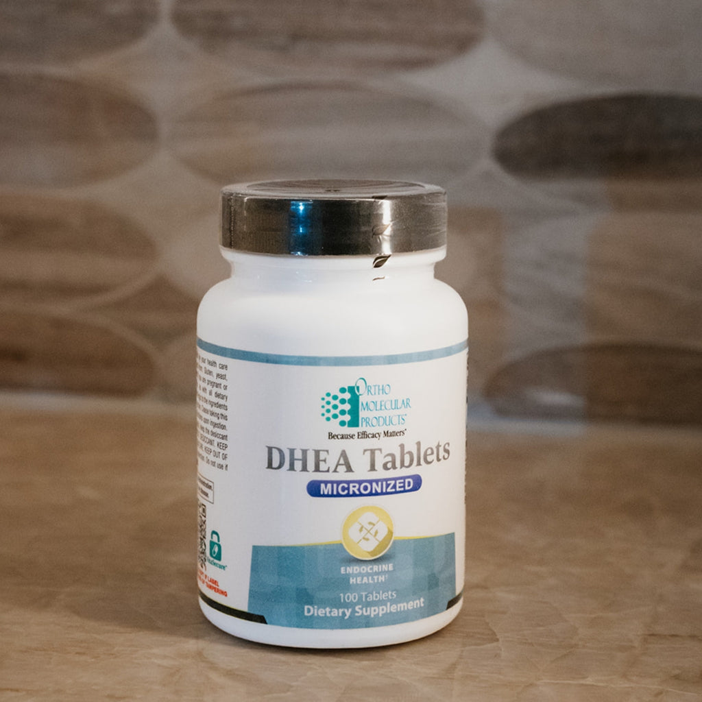 A bottle of Oho Kuling Products DHEA Tablets Micronized dietary supplement, set against a blurred stone-tile background.