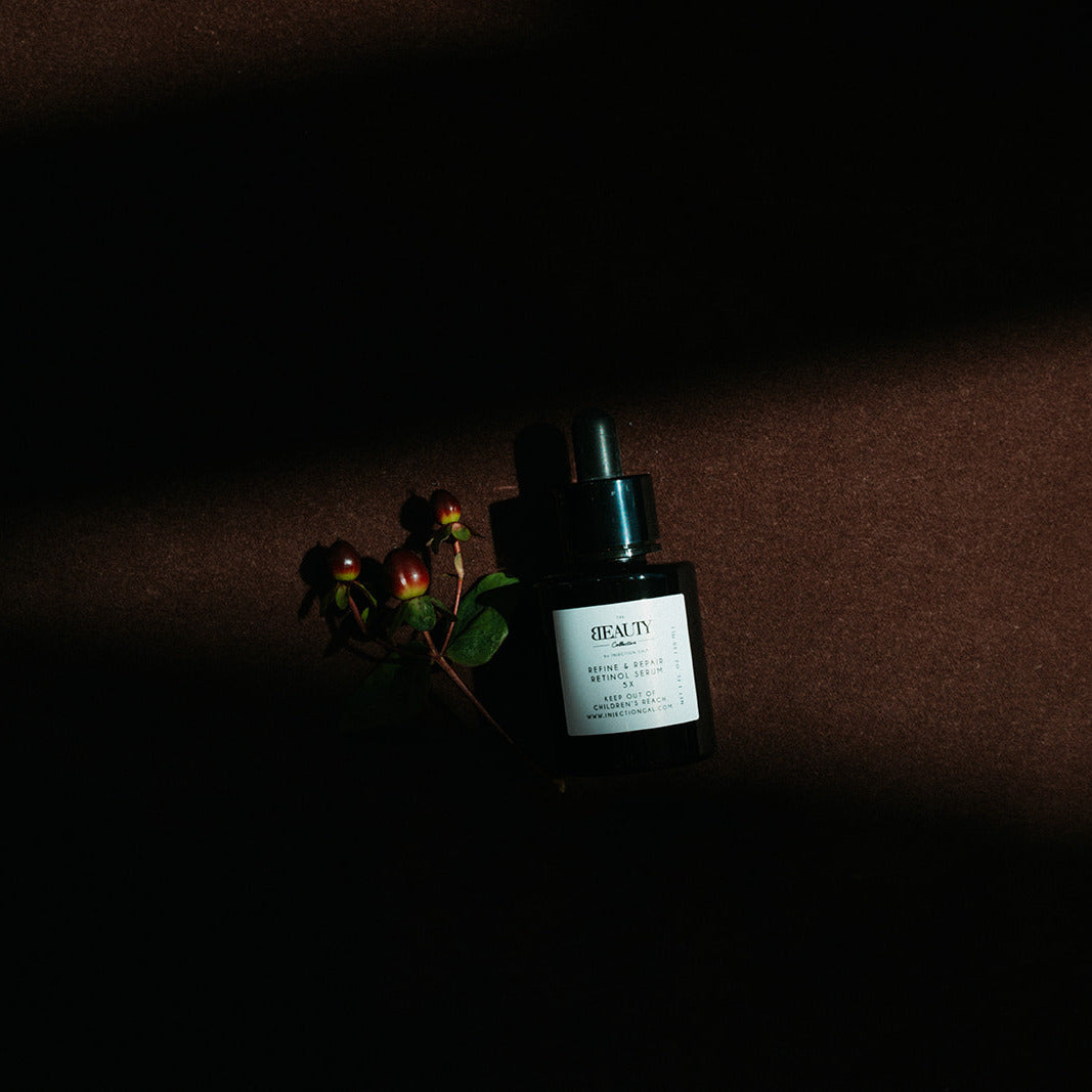 A dark amber glass dropper bottle with a white label reading 'BEAUTY' and botanical stems, photographed in dramatic low light against a dark brown background.