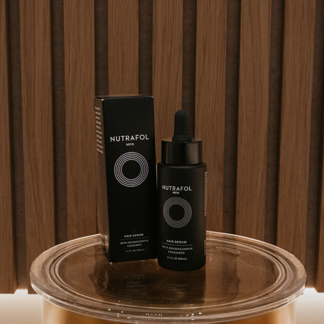 NUTRAFOL Men Hair Serum 10ml bottle and its black packaging box, displayed on a reflective metallic surface against a dark wood slatted background.