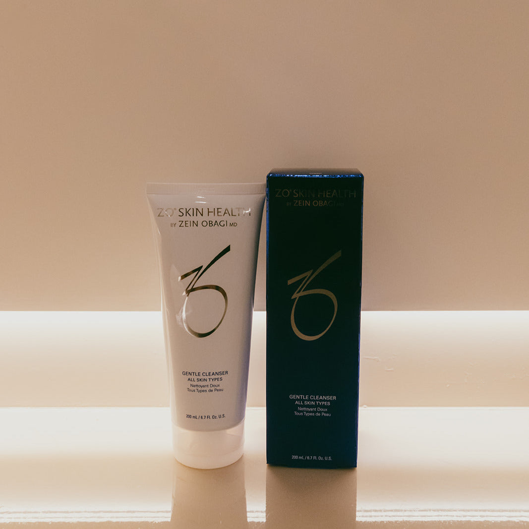 ZO Skin Health Zein Obagi Gentle Cleanser All Skin Type in a white squeeze tube next to its dark teal-blue box, set against a warm beige background.