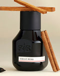 Black perfume bottle labeled 'Calle Ocho' with cinnamon sticks on a beige background